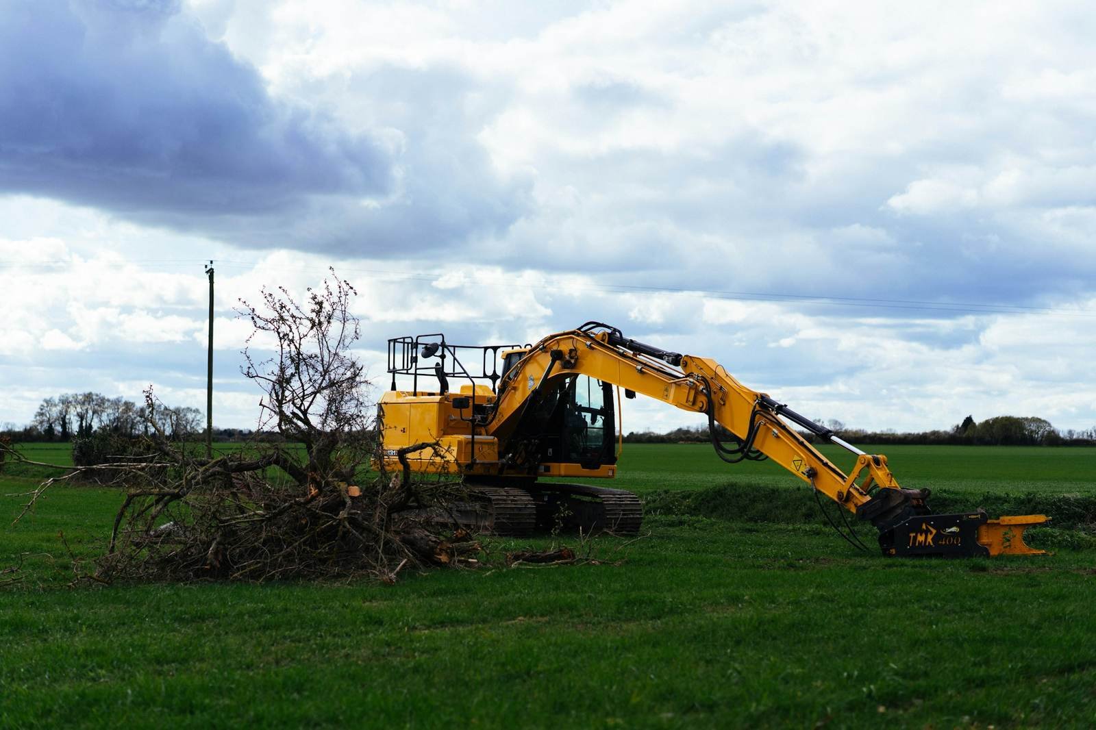 Excavator clearing brush and branches from an open field