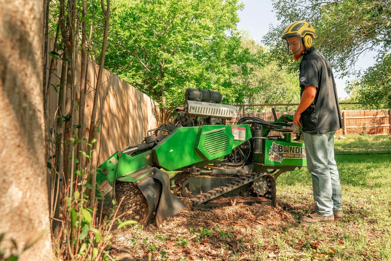 Worker running a stump grinder next to a backyard fence